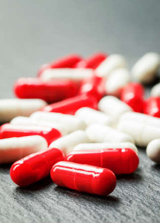 Painkillers pills in red and white capsules on dark background, macro shot, selective focus, shallow...