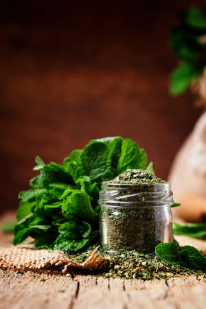 Dried peppermint in a glass jar and a bunch of fresh mint, vintage wood background, selective focus