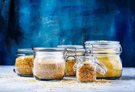 Assorted cereals in glass jars: kinoa, bulgur, couscous, orzo, brown rice, selective focusの写真素材