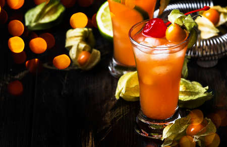Alcoholic cocktail with vodka, liqueur, bitter, lime juice, decorated with physalis and maraschino cherries, dark background, selective focusの写真素材