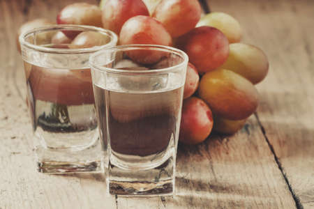 Grapple in small glass and ripe grapes on old wooden table, selective focusの写真素材