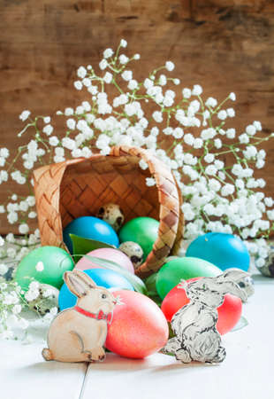Happy easter! Festive composition with colored eggs, poured out of a wicker basket, painted rabbits, white flowers, selective focusの写真素材