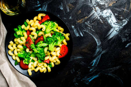 Cooked vegetarian pasta with broccoli and tomatoes, dark background, top viewの写真素材
