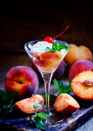 Dessert of peaches and yoghurt in martini glass, dark wood background, low key, selective focusの写真素材