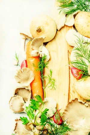 Food background, ingredients for cooking soup with oyster mushrooms, potatoes, vegetables and herbs, wooden cutting board, gray background, top viewの写真素材