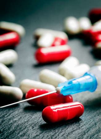 Red and white tablets in capsules, syringe for injection, dark background, selective focus, shallow depth of fieldの写真素材