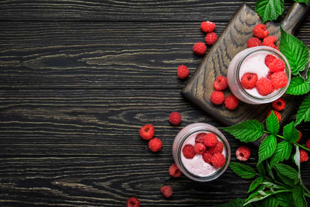 Raspberry smoothie in glass jars with fresh berry and yogurt on vintage wooden kitchen table...