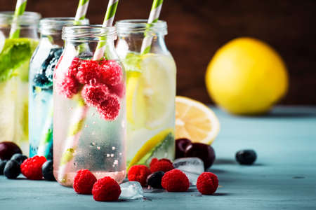 Berry, fruit and citrus non-alcoholic cold drinks and cocktails in glass bottles on blue background,...