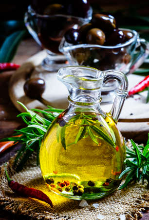 Olive oil with rosemary and spices in a glass jug, vintage wooden background, selective focusの写真素材