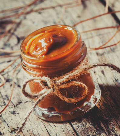 Soft homemade caramel in a glass jar on the old wooden table in rustic style, selective focus and toned imageの写真素材