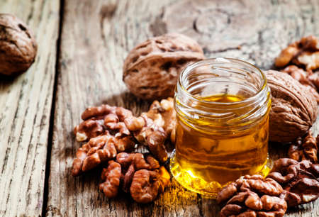 Walnut oil in a small jar and kernels on old wooden background in rustic style, selective focusの写真素材