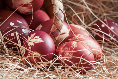 Brown painted Easter eggs with natural grass pattern spill out of a wicker basket on an old wooden background with straw, still life in rustic style, selective focusの写真素材