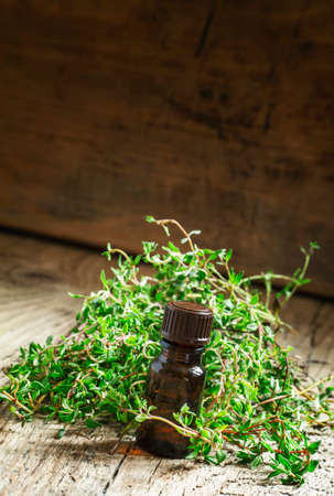 Essential oil of thyme in a bottle and fresh herb thyme on an old wooden background, selective focusの写真素材