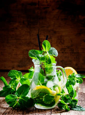 Summer citrus lemonade with peppermint, lemon, green tea and ice cubes in a glass pitcher, vintage wooden background, selective focusの写真素材