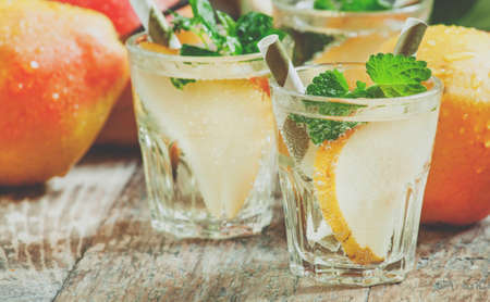 Pear cocktail with soda, fruit slices and mint on an old wooden table, selective focus and toned imageの写真素材