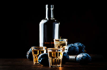 Slivovica - plum brandy or plum vodka, hard liquor, strong drink in glasses on old wooden table, fresh plums, copy spaceの写真素材