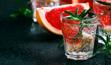 Alcoholic cocktail with grapefruit, soda, ice, gin and rosemary, dark stone bar counter background, selective focusの写真素材