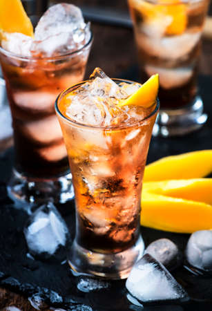 Alcoholic cocktail with mango, cranberries, lime, crushed ice and liquor, dark wooden bar counter...