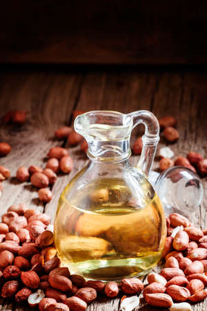 Peanut oil in a glass jar, raw peanuts, vintage wooden background, selective focus