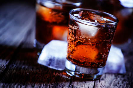 Alcoholic cocktail bourbon cola with whiskey and ice cubes, vintage wooden background, selective focusの写真素材
