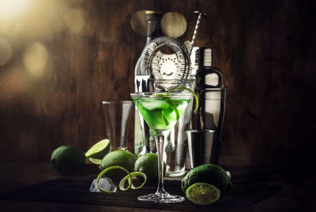 Green martini alcoholic cocktail in glass with dry gin, vermouth, liquor, lime zest and ice, steel...