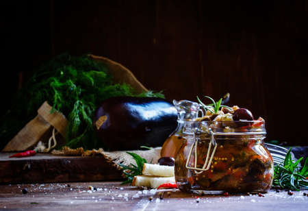 Homemade Eggplant Caponata with black olives in a glass jar, vintage wooden background, selective...