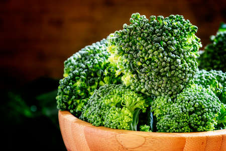 Fresh green broccoli in a wooden bowl on dark wooden background, selective focusの写真素材