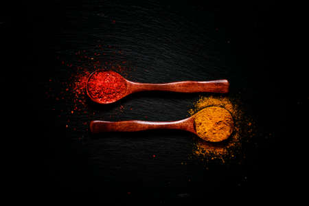 Curry and chili pepper spices, wooden spoons, black stone background, food background, top view