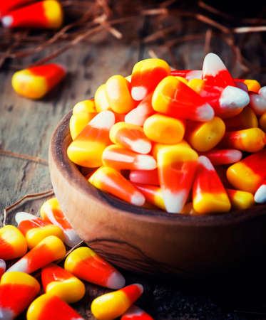 Halloween festive composition with sweet corn in bowl and smiling pumpkins guards, lantern, straw and fallen leaves on dark wooden background, rustic style, selective focusの写真素材