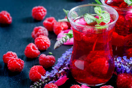 Herbal red tea with raspberries, mint, sage flowers and rose petals in the eastern glasses on dark...