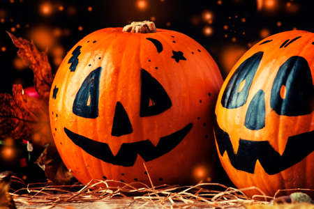 Halloween festive composition with smiling pumpkins guards, lantern, straw and fallen leaves on dark...