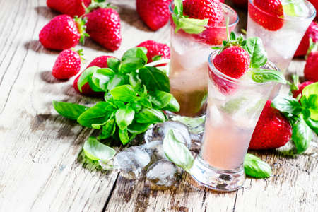 Pink cocktail with strawberry, basil, gin and ice, wood background, selective focusの写真素材