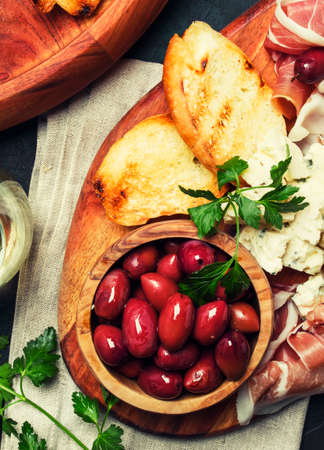 Snacks or antipasti, crostini, prosciutto, blue cheese and olives, black background, top viewの写真素材
