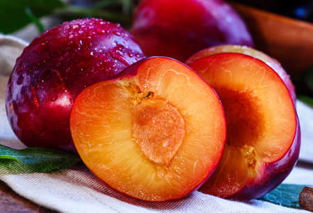 Red plums, cut in half, vintage wooden background, rustic style, selective focus