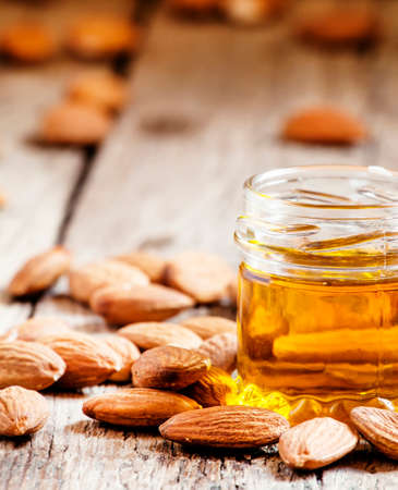 Sweet Almond Oil, first extraction, in a small glass jar, dry almond nuts on an old wooden background, selective focusの写真素材