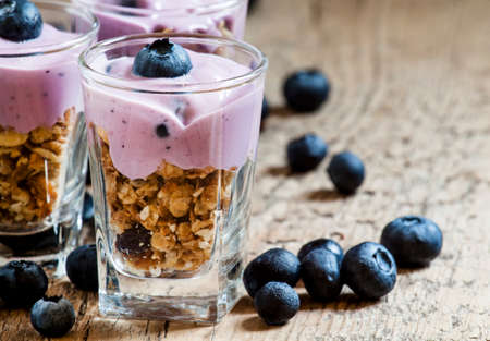 Homemade baked granola with yogurt and blueberries in a glass and old wooden background, selective focusの写真素材