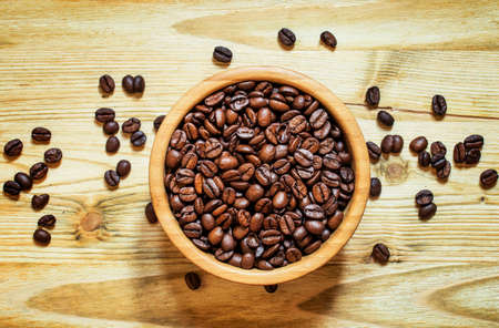 Grains of roasted coffee in a round bowl on a wooden background, top view
