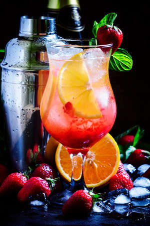 Alcoholic cocktail with sparkling white wine, strawberries, oranges and ice, black background,...