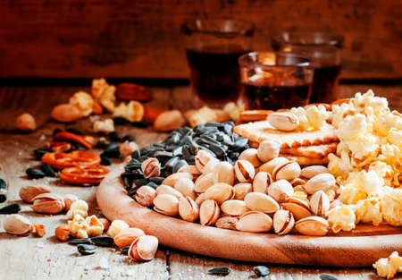 Salted pistachios, popcorn and other salty snacks on a wooden platter, selective focusの写真素材