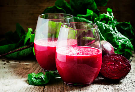 Beetroot smoothie in a large glass, fresh beets with tops, old wooden background, selective focus