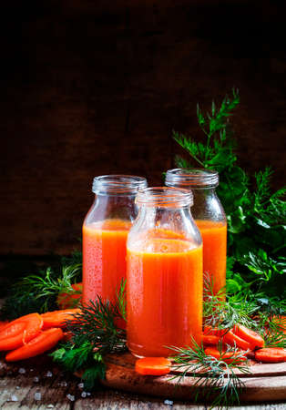 Freshly squeezed juice of carrots in glass bottles, vintage wooden background, selective focusの写真素材