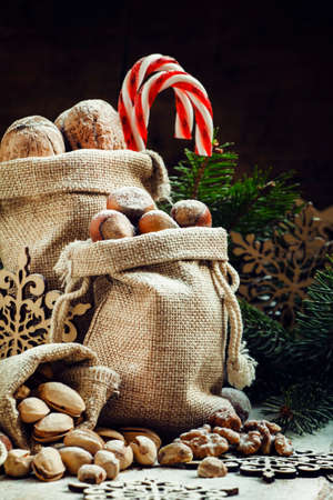 New Year or Christmas composition with walnuts, hazelnuts, pistachios in canvas bags with fir branches and cones. Vintage wood background, selective focusの写真素材