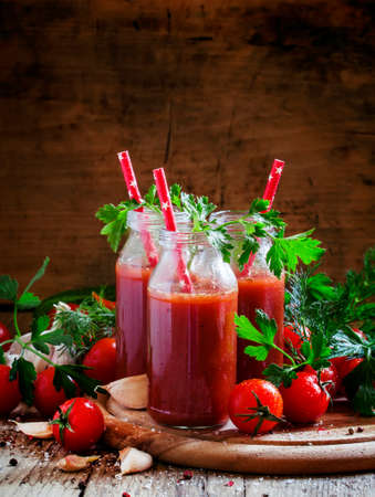 Smoothies of tomatoes and spices in glass bottles with festive red drinking straws, selective backgroundの写真素材