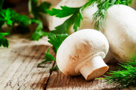 White mushrooms champignons, dill, parsley, old wooden table, rustic style, selective focusの写真素材