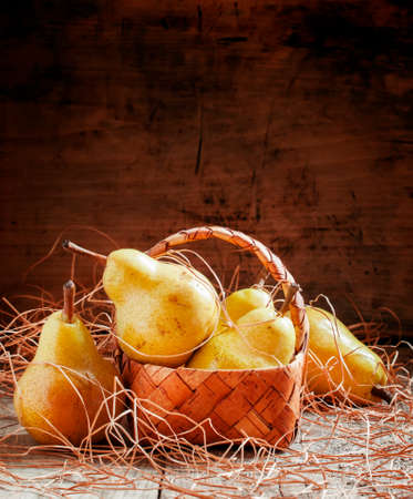 Ripe yellow pears in a wicker basket on an old wooden background in country style, selective focusの写真素材