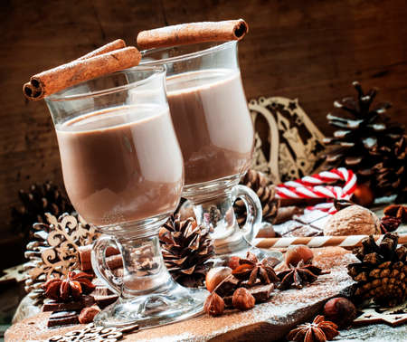 Cocoa in large glasses for hot drinks in Christmas decorations with spices, pine cones and snowflakes, vintage wooden background, selective focusの写真素材