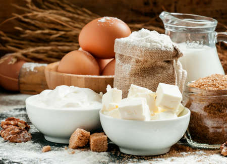 Baking ingredients: milk, butter, flour, sugar, eggs and rolling pin on a floured table in a rustic...