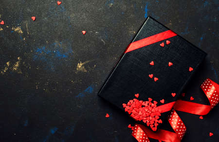 Gift for man on Valentines day, black box with red ribbon and sweet hearts, dark background, top...