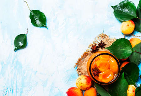 Apricot jam with anise stars and fresh apricots with leaves, top view