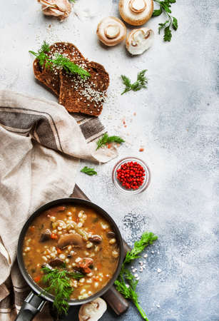 Autumn or winter meat vegetable mushroom hot soup with beef and wholegrain barley. With black brew and parsley, top view, gray kitchen table, copy spaceの写真素材